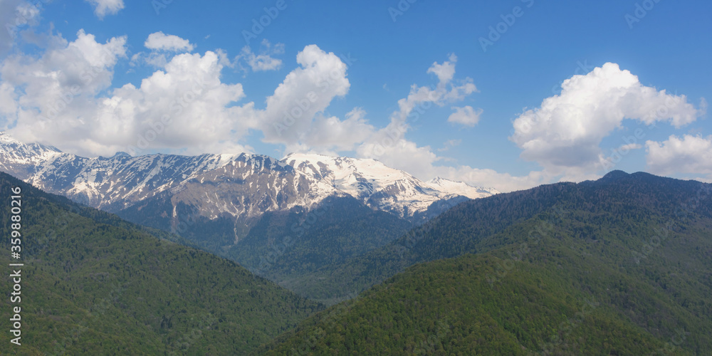 Mountains with snow and forest panorama. Beautiful landscape of the Caucasus mountain range in April. The spring mountains. A long narrow natural banner. Travel to Russia.