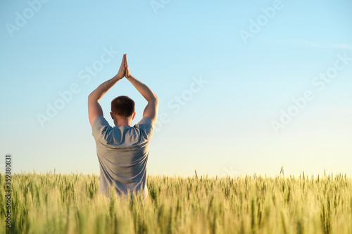 Fototapeta Naklejka Na Ścianę i Meble -  Adult man stands on a field in tall grass doing yoga during sunrise. Mental health, connection with nature concept. Space for text.