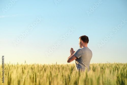 Adult man stands on a field in tall grass doing yoga during sunrise. Mental health, connection with nature concept. Copy space.