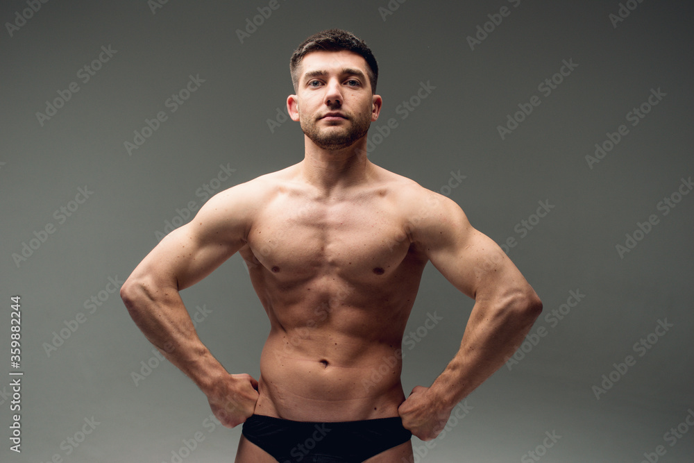 Dramatic studio portrait of attractive handsome young male bodybuilder or athlete posing in black underwear isolated on black background