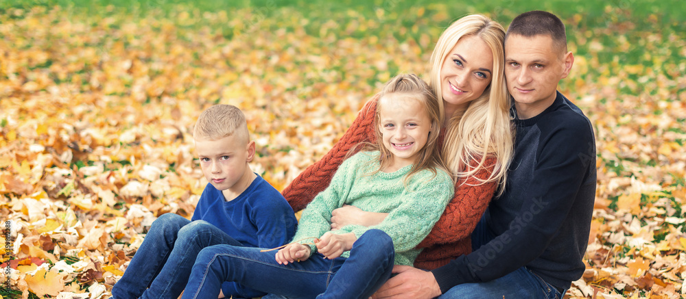 Fototapeta premium Portrait of young family sitting in autumn leaves. Parents with children sitting in the autumn park