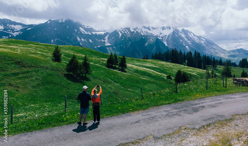 Aerial view of couple in love of travellers admiring beauty of picturesque Alpine mountains. Two romantic wanderlusts traveling around world together. Tourist photographing breathtaking view on phone