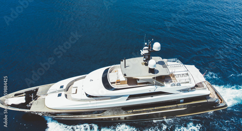 Aerial view of luxury yacht goes to open sea with beautiful blue colour of water. Wealth recreation lifestyle. Bird's eye view of expensive floating ship traveling by Europe in summer