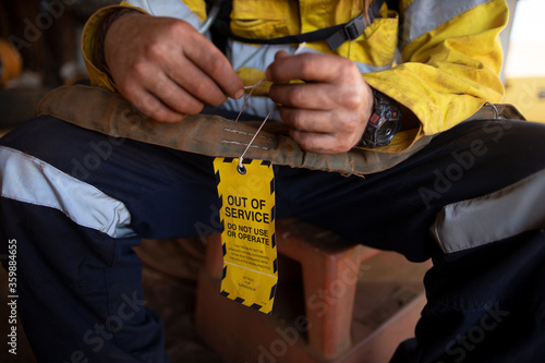 Safety workplaces trained competent person inspecting and attached yellow out of service tag on faulty damage defect on 2 ton green lifting sling at construction site Perth, Australia