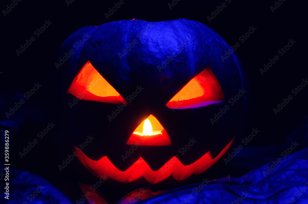 Glowing pumpkin with a candle inside close-up in the foliage with blue illumination. Halloween decorations, background. Glowing pumpkin with a candle inside close-up in the foliage with blue illumination. Halloween decorations, background.