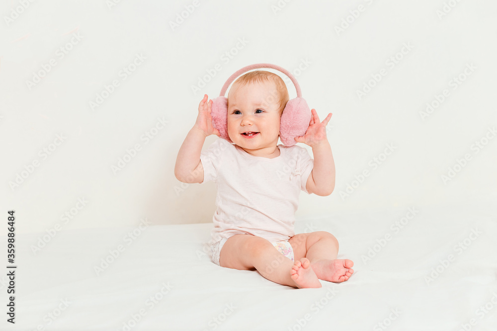 Smiling baby in a diaper and fur headphones sits on the bed Smiling baby in a diaper and fur headphones sits on the bed