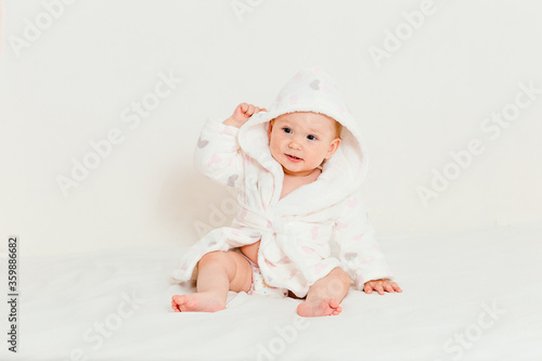 Baby in a bathrobe after bathing sits on a bed
