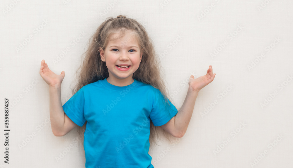 Portrait of a funny blond little girl in a blue T-shirt who smiles and laughs isolated on a white (light) background. Hands up. copy space.