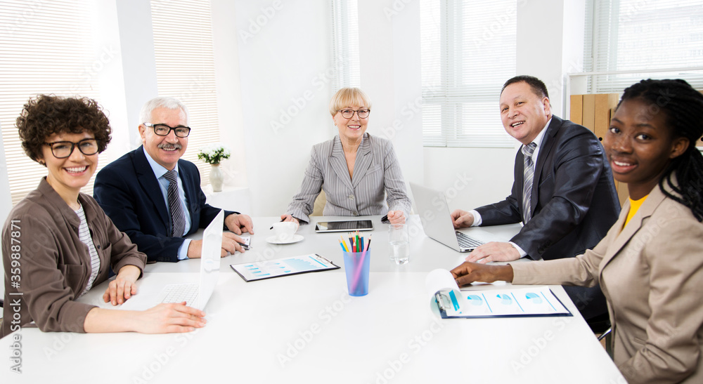Multy-ethnic group of business people sitting at the office desk and smiling at camera Multy-ethnic group of business people sitting at the office desk and smiling at camera