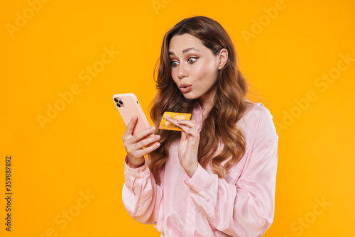 Image of nice surprised woman holding credit card and mobile phone