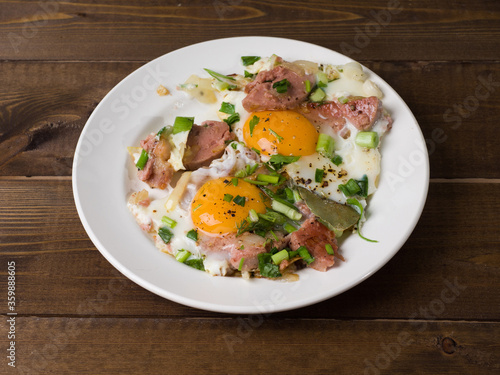 Homemade fried eggs with sausage and herbs. White plate on wooden boards