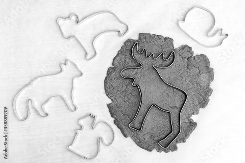 White and black photo of moose-shaped cookie mold lies on a small rolled piece of brown dough