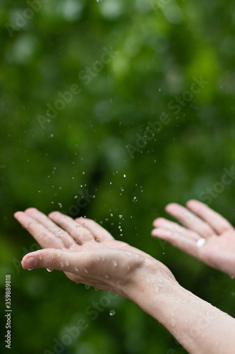 Catching rain drops. Man hand in the rain on the green nature background.