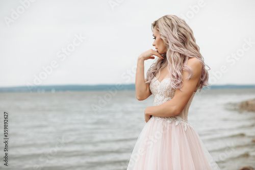 young beauty on the beach with a view of the sea. Sensual portrait of a sexy bride with loose hair in a soft pink dress