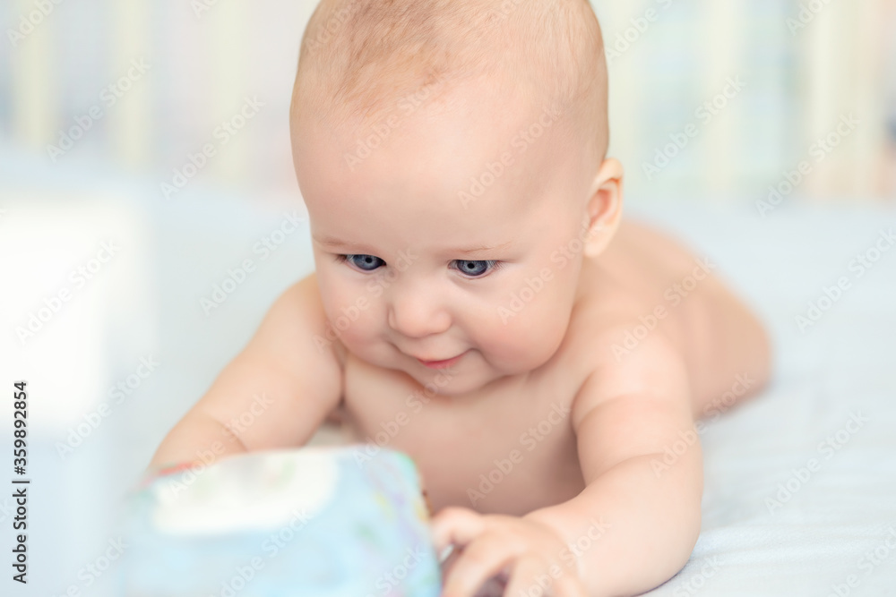 Cute adorable caucasian little 5 month old infant baby boy lying on tummy at nursery bed room having fun playing and smiling. Happy healthy newborn child concept. Funny toddler kid closeup portrait