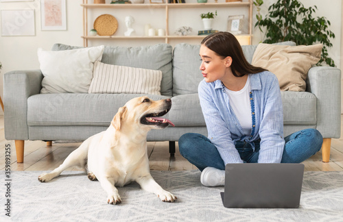 Young woman at home with laptop and a dog © Prostock-studio