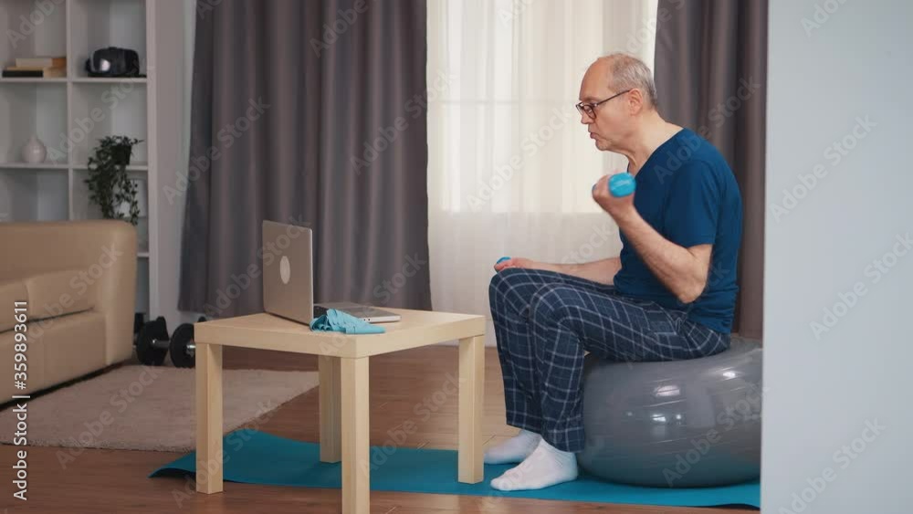 Senior man training in living room with dumbbells during online fitness program. Old person pensioner healthy training healthcare sport at home, exercising fitness activity at elderly age Senior man training in living room with dumbbells during online fitness program. Old person pensioner healthy training healthcare sport at home, exercising fitness activity at elderly age