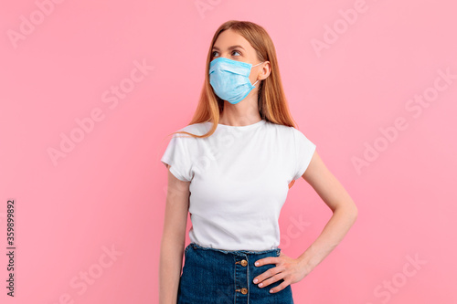 Pensive girl in a medical protective mask on her face, on a pink background. Coronavirus epidemic, quarantine