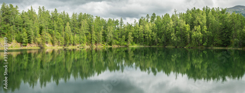 Wild forest lake, panoramic view. Gloomy sky, beautiful reflection. Travel and summer vacation.