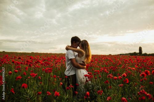 Obraz na płótnie Romantic young couple hug among red beautiful poppy field. Freedom, family and love concept. Man and woman enjoy spending time together among red flowers. Copy space. w salonie