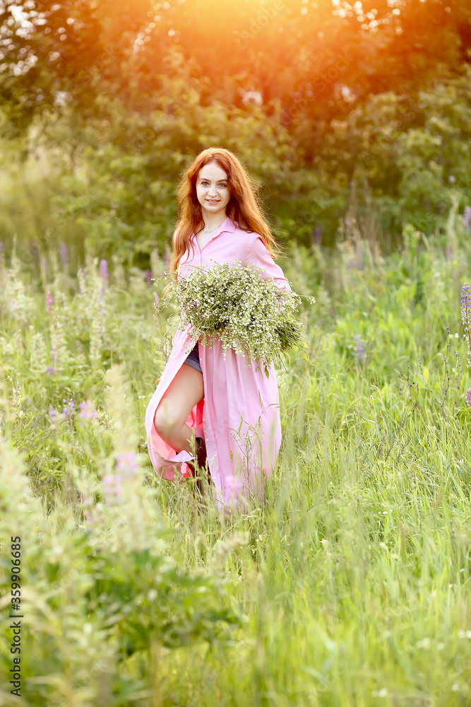 Young beautiful red-haired girl in a pink dress with a huge bouquet of daisies runs summer in the garden at sunset. The effect of bokeh, flash, sun rays. Summer concept. Copy space Young beautiful red-haired girl in a pink dress with a huge bouquet of daisies runs summer in the garden at sunset. The effect of bokeh, flash, sun rays. Summer concept. Copy space