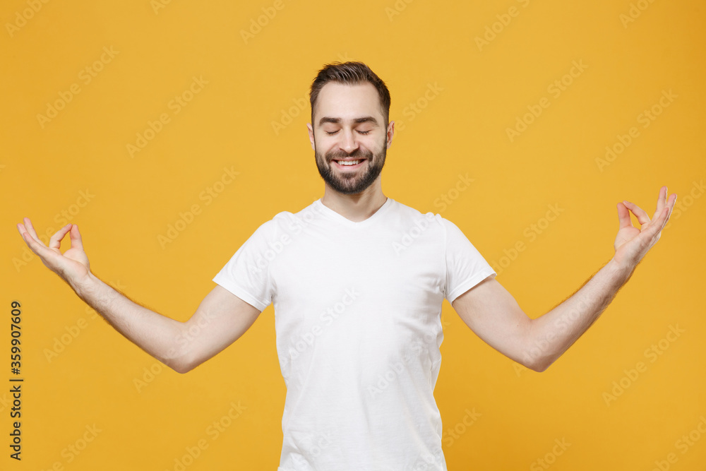 Smiling young bearded guy in white casual t-shirt posing isolated on yellow background studio portrait. People lifestyle concept. Mock up copy space. Hold hands in yoga gesture, relaxing meditating. Smiling young bearded guy in white casual t-shirt posing isolated on yellow background studio portrait. People lifestyle concept. Mock up copy space. Hold hands in yoga gesture, relaxing meditating.