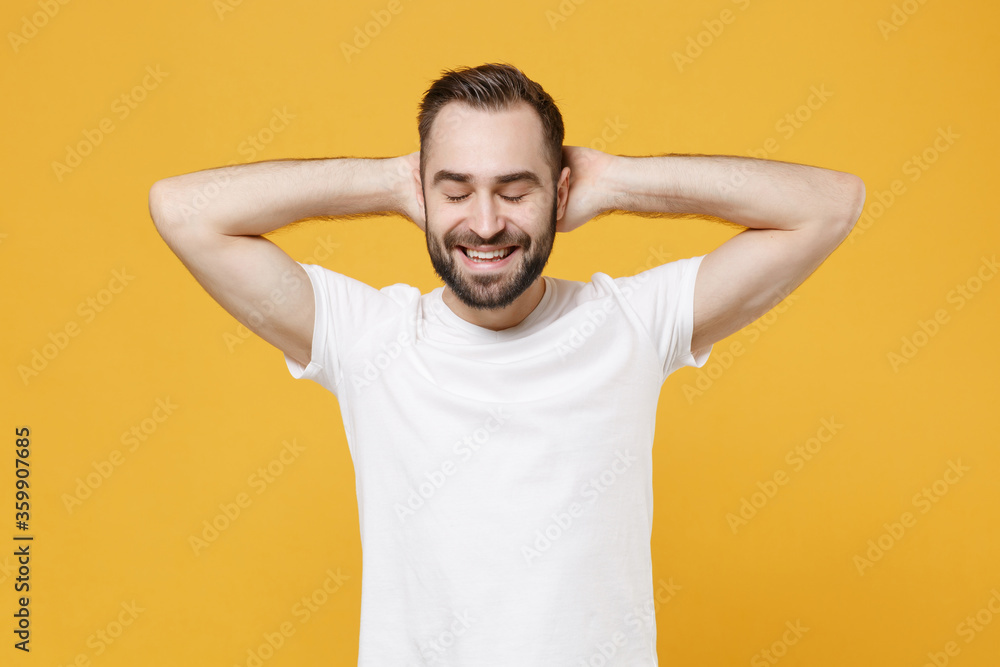 Smiling young bearded man guy in white casual t-shirt posing isolated on yellow wall background studio portrait. People emotions lifestyle concept. Mock up copy space. Sleep with hands behind head. Smiling young bearded man guy in white casual t-shirt posing isolated on yellow wall background studio portrait. People emotions lifestyle concept. Mock up copy space. Sleep with hands behind head.
