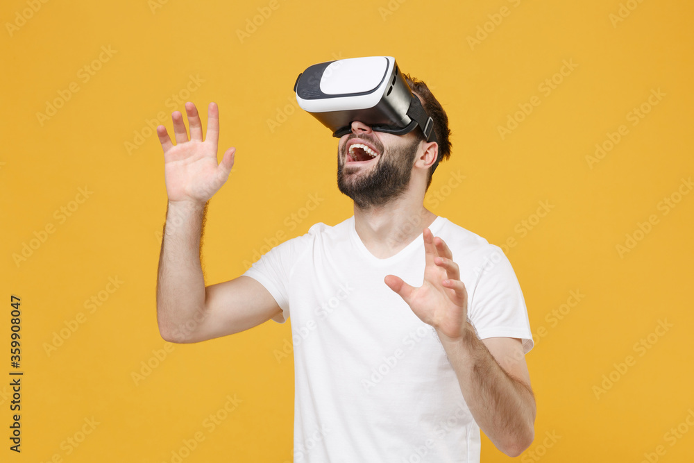 Excited young bearded man guy in white casual t-shirt posing isolated on yellow background studio. People lifestyle concept. Watching in headset touch something push on button point at virtual screen. Excited young bearded man guy in white casual t-shirt posing isolated on yellow background studio. People lifestyle concept. Watching in headset touch something push on button point at virtual screen.