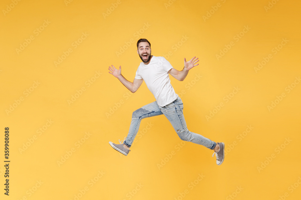 Excited young bearded man guy in white casual t-shirt posing isolated on yellow background studio portrait. People emotions lifestyle concept. Mock up copy space. Jumping spreading hands and legs.