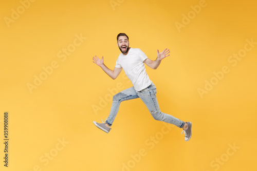 Excited young bearded man guy in white casual t-shirt posing isolated on yellow background studio portrait. People emotions lifestyle concept. Mock up copy space. Jumping spreading hands and legs. © ViDi Studio
