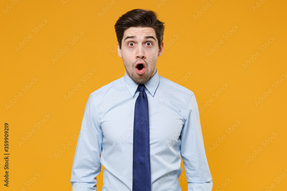 Shocked young business man in classic blue shirt tie posing isolated on yellow wall background studio portrait. Achievement career wealth business concept. Mock up copy space. Keeping mouth open. Shocked young business man in classic blue shirt tie posing isolated on yellow wall background studio portrait. Achievement career wealth business concept. Mock up copy space. Keeping mouth open.