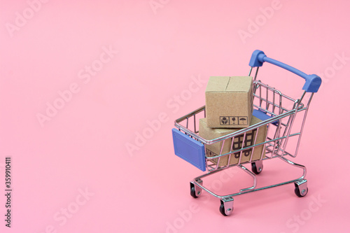 Shopping concept : Cartons or Paper boxes in blue shopping cart on pink background. online shopping consumers can shop from home and delivery service. with copy space.
