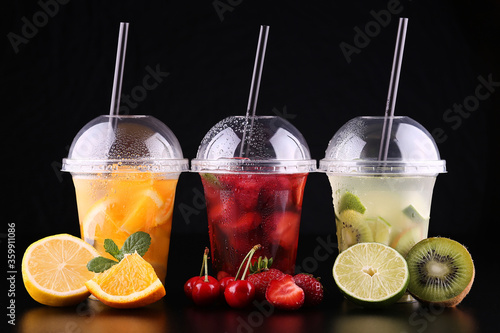 Lemonade to go. Three cups with mint, cherry, strawberry, kiwi, lime, orage, lemon on black background, isolated