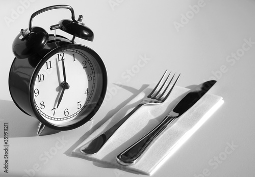 Alarm clock with fork and knife. Time to eat. Weight loss or diet concept. An image of a retro clock showing 7:00 am/pm. 