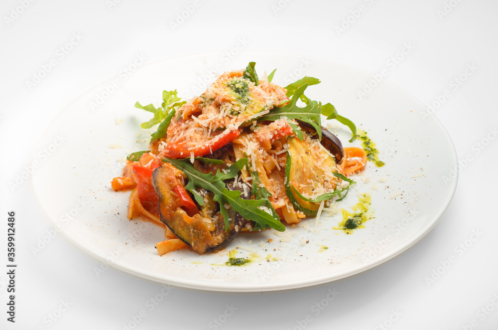 Tagliatelle with grilled vegetables and pesto. Beautiful serve on a white plate, on a white background. For use in menu design and food delivery service.
