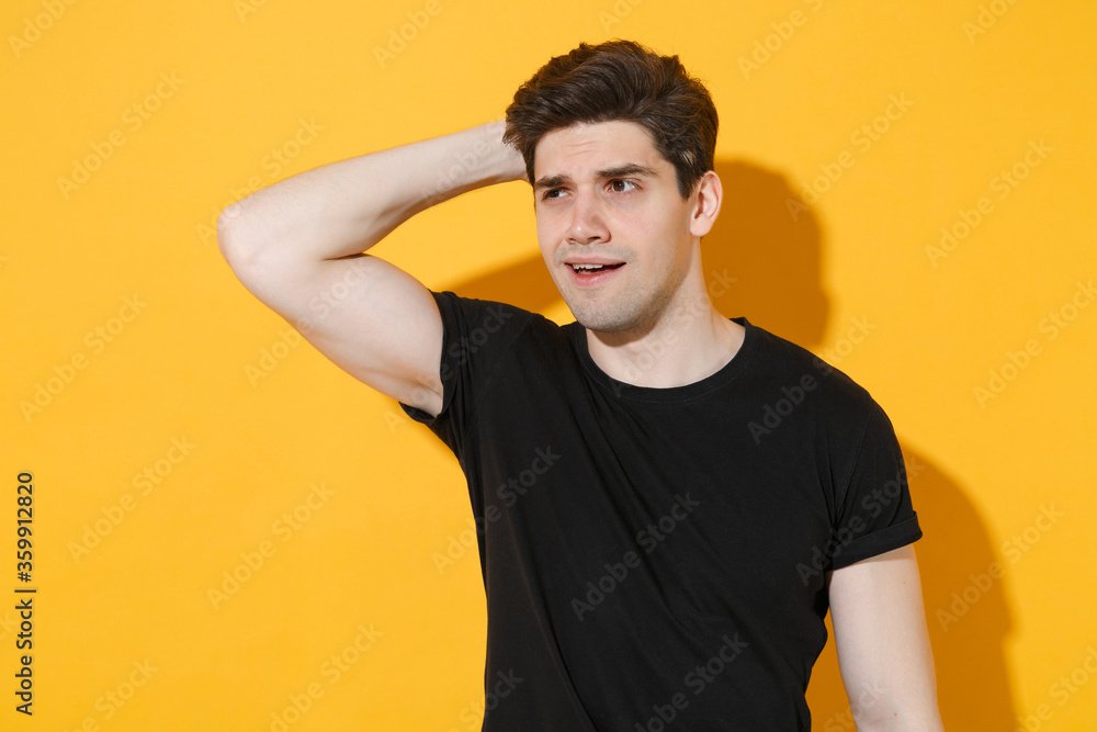 Preoccupied young man guy in casual black t-shirt posing isolated on yellow background studio portrait. People sincere emotions lifestyle concept. Mock up copy space. Put hand on head, looking aside. Preoccupied young man guy in casual black t-shirt posing isolated on yellow background studio portrait. People sincere emotions lifestyle concept. Mock up copy space. Put hand on head, looking aside.