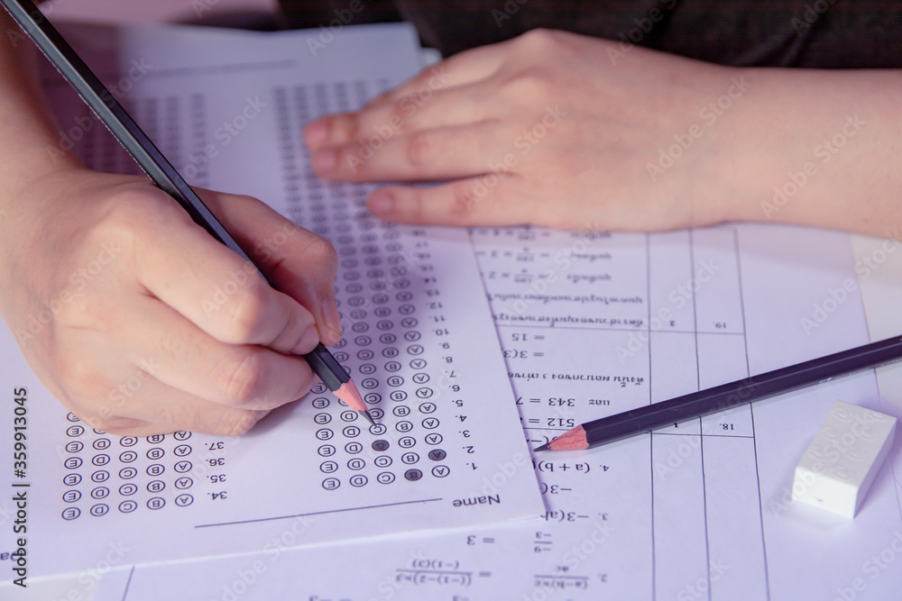 Students hand holding pencil writing selected choice on answer sheets and Mathematics question sheets. students testing doing examination. school exam. Students hand holding pencil writing selected choice on answer sheets and Mathematics question sheets. students testing doing examination. school exam.