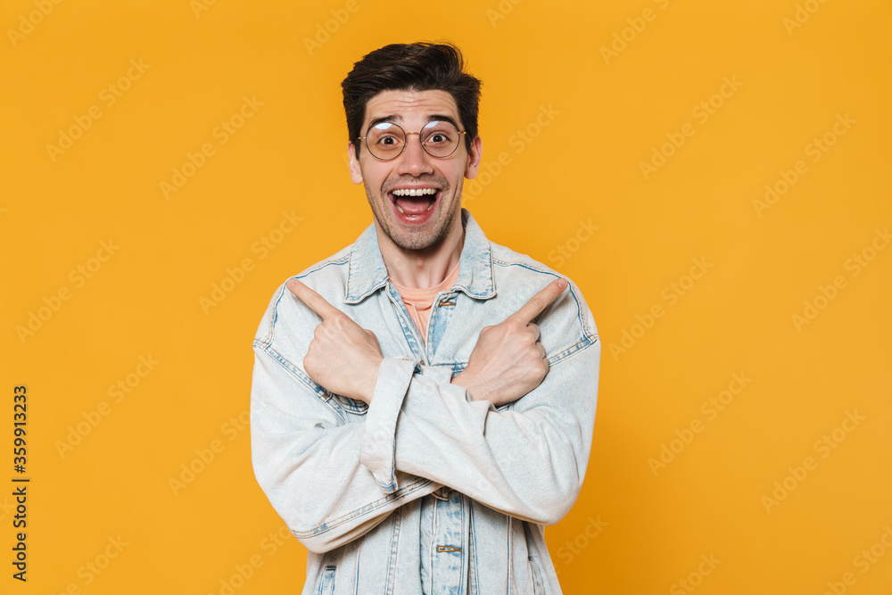 Photo of delighted young man in eyeglasses pointing fingers aside Photo of delighted young man in eyeglasses pointing fingers aside