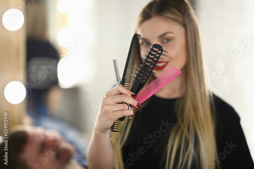 Close up of charming female hairdresser demonstrating hairstyling tools and smiling