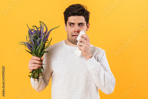 Photo of unhappy man with allergy crying while posing with flowers