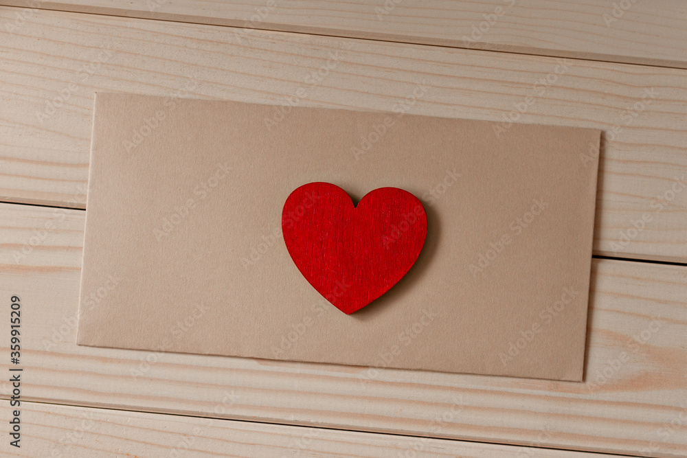 red wooden small heart lies on a brown envelope on wooden table diagonally red wooden small heart lies on a brown envelope on wooden table diagonally