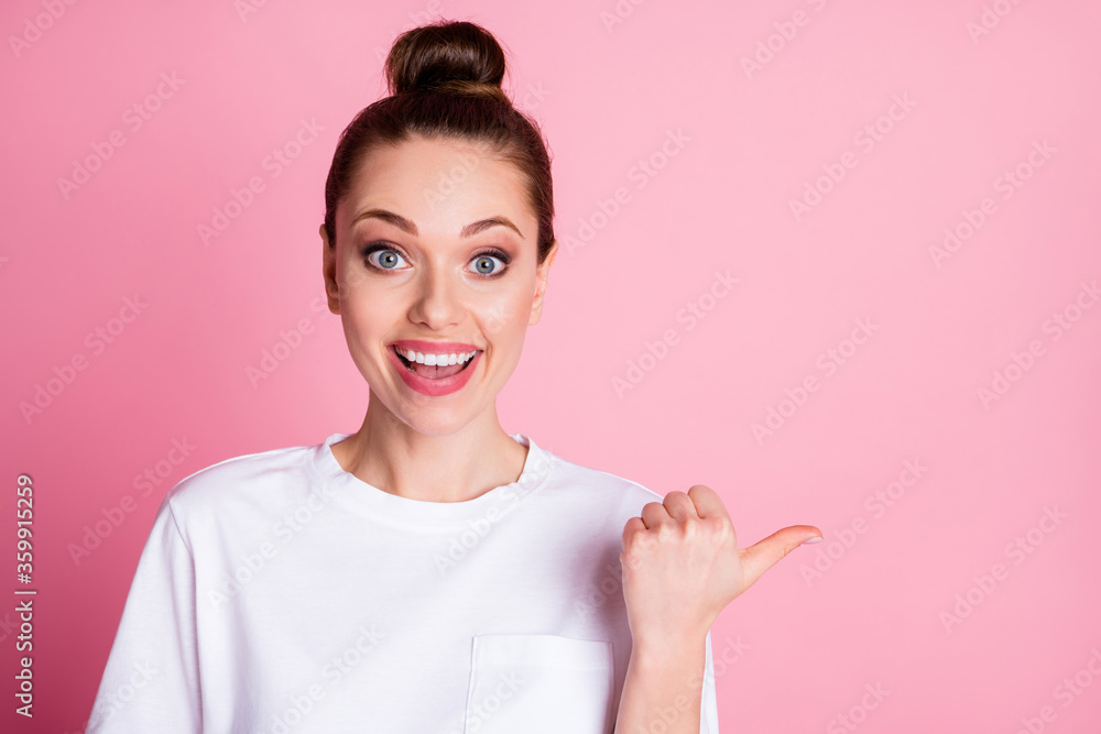Closeup photo of attractive lady funny bun hairdo direct thumb finger side empty space show sale discount proposition shopping season wear white t-shirt isolated pastel pink color background Closeup photo of attractive lady funny bun hairdo direct thumb finger side empty space show sale discount proposition shopping season wear white t-shirt isolated pastel pink color background