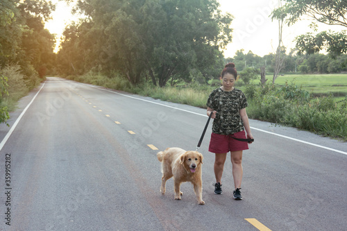 Asian woman with her golden retriever dog walking on the public road..