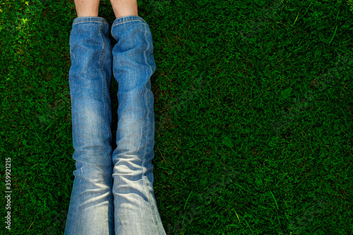 legs of a girl in blue jeans sitting on green grass on a lawn, top view, flat lay