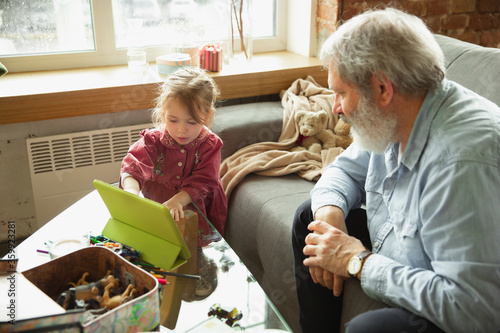 Grandfather and grandchild playing together at home. Happiness, family, relathionship, learning and education concept. Sincere emotions and childhood. Reading books, fairytails, poems, look happy. photo