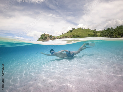Fototapeta Naklejka Na Ścianę i Meble -  Half water view of man diving. pink sand at Komodo island, Indonesia.