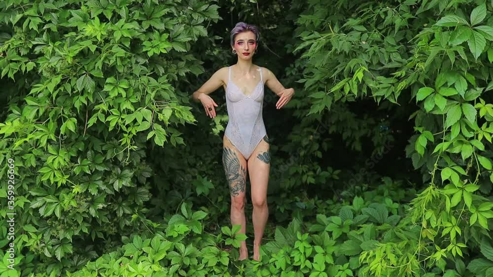 stylish girl with bright short hair, lenses in her eyes and piercings and tattoos in a white bodysuit against the background of nature stylish girl with bright short hair, lenses in her eyes and piercings and tattoos in a white bodysuit against the background of nature