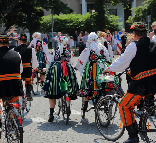 Local people in traditional folk costumes from Lowicz, Poland, ride bicycles in street while celebrate Corpus Christi holiday
