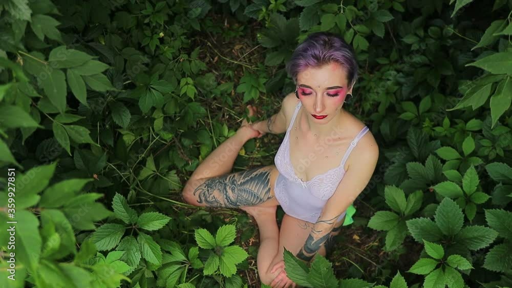 stylish girl with bright short hair, lenses in her eyes and piercings and tattoos in a white bodysuit against the background of nature stylish girl with bright short hair, lenses in her eyes and piercings and tattoos in a white bodysuit against the background of nature