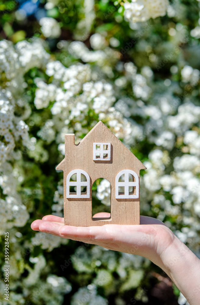The girl holds the house symbol against the background of white flower The girl holds the house symbol against the background of white flower